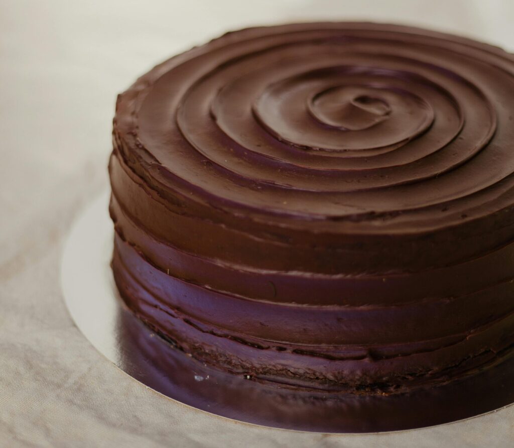 A rich, round chocolate cake with smooth frosting on a rustic light-colored surface.