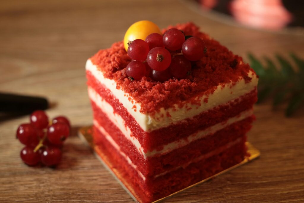 Delicious red velvet cake slice with cream cheese frosting and fresh berries on top.
